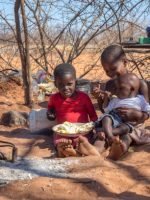 two african children in a village near Kalahari desert, the sister feeding her brother in the outdoors kitchen